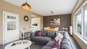 Ein modernes Wohnzimmer mit grauem Sofa, einem weißen Couchtisch und einem Essbereich mit Holztisch und Stühlen.
