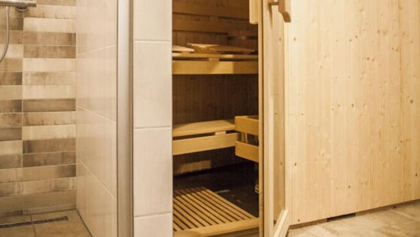 Een sauna met een houten deur, een betegelde muur en een bankje.