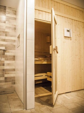 Una sauna con porta in legno, parete rivestita di piastrelle e una panca all'interno.