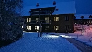 Een meerlaags gebouw met balkon, sneeuw bedekte grond en een heldere lucht.