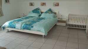 Un dormitorio con una cama, mesitas de noche, una cuna y una pared decorada con tres pequeños cuadros.