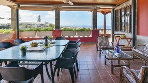 A covered patio with a table and chairs, a sofa, and a view of the sea. - Villa in Gran Canaria With Private Pool & Tennis (Arucas)