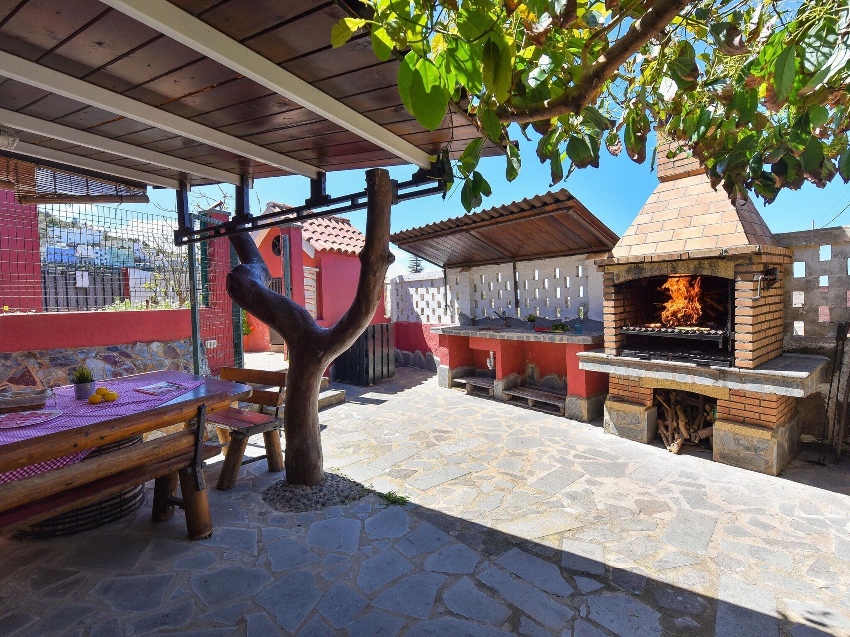 Patio esterno con barbecue in mattoni, pavimento in pietra e tavolo di legno con un sottotavolo viola.