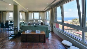A spacious living area with a large window offering a view of the sea. There is a sofa set, a coffee table, and a dining area with chairs. - Villa in Gran Canaria With Private Pool & Tennis (Arucas)