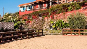 A large, red-roofed building with multiple balconies, surrounded by lush greenery and a sandy area in the foreground. - Villa in Gran Canaria With Private Pool & Tennis (Arucas)