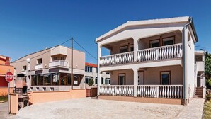 A two-story building with a balcony, a stop sign, and a stone-paved area. - Apartments Hak - One Bedroom Apartment With Terrace and Sea View (Vir)