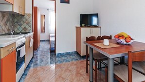 A compact kitchen with modern appliances, a dining area with a table and chairs, and a television on a cabinet. - Apartments Hak - One Bedroom Apartment With Terrace and Sea View (Vir)