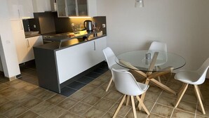 A modern kitchen with white cabinets, a black countertop, and a glass dining table with white chairs. - Holiday Apartment Casa Chimp 5 (Gambarogno)