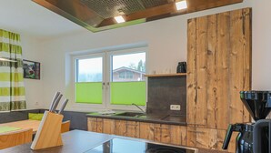 A modern kitchen with a built-in stove, wooden cabinets, and a window with a view of a house. - Apartment in Brixen Near Ski Welt (Brixen im Thale)
