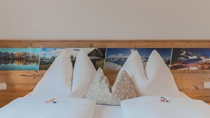 A bed with white bedding and decorative pillows, a wooden headboard, and a series of framed landscape photographs above. - Apartment in Brixen Near Ski Welt (Brixen im Thale)