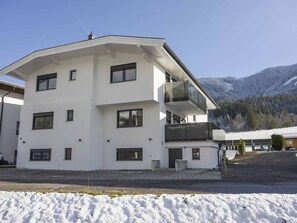 A multi-story white building with balconies, a paved driveway, and a snow-covered landscape with mountains in the background.