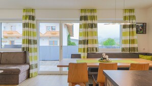 A modern living room with a sofa, dining table, chairs, and a view of the outside. - Apartment in Brixen Near Ski Welt (Brixen im Thale)
