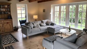 A cozy living room with a grey sectional sofa, a small round table with a bottle, and a bookshelf filled with books. - Appelhus Modern Retreat (Loit)