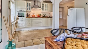 A kitchen with white cabinets, a stove, and a refrigerator. There is a wooden table with baked goods in the foreground. - Appelhus Modern Retreat (Loit)
