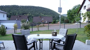 An outdoor patio with a round table and four chairs, surrounded by a fence, with houses and a hill in the background. - Haus Edith Modern Retreat (Lug)
