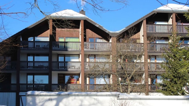 Un edificio a più piani con balconi, un tetto imbiancato dalla neve e un cielo azzurro limpido.