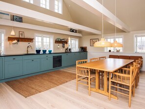 A modern kitchen with teal cabinets, a wooden dining table, and pendant lights. - 6 Person Holiday Home in Fano (Fano)