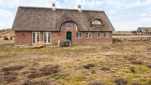 A thatched-roof house with a brick exterior, a green door, and a small porch with two chairs. - 6 Person Holiday Home in Fano (Fano)