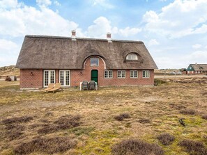 A thatched-roof house with a brick exterior, a green door, and a small porch with two chairs. - 6 Person Holiday Home in Fano (Fano)