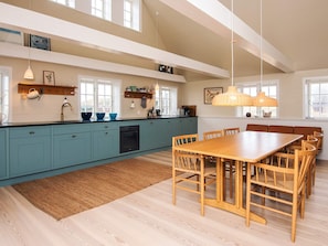 Een moderne keuken met een groot eiland, lichtblauwe kastjes en een houten eettafel met stoelen.