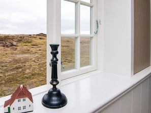 Een raam met uitzicht op een begroeiend landschap, een zwart object op de vensterbank, en een klein modelhuis.