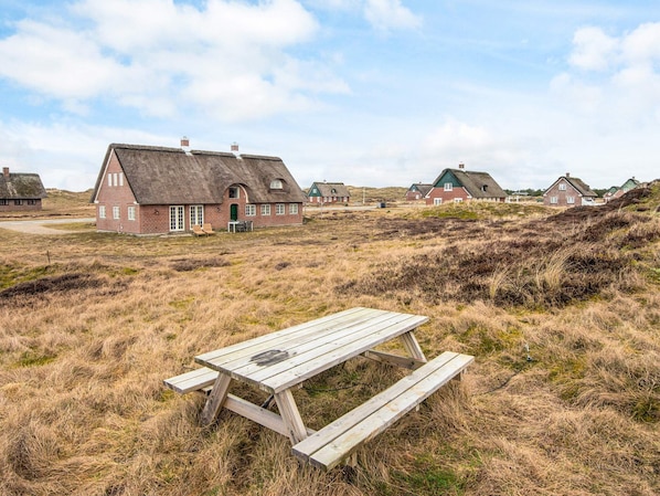 A rural setting with traditional thatched-roof houses, a wooden picnic table, and a grassy landscape.