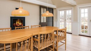 A dining area with a long wooden table and chairs, two hanging wicker lamps, a fireplace with a fire, and a large sliding glass door leading to an outdoor area. - 6 Person Holiday Home in Fano (Fano)