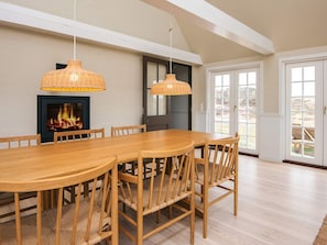 A dining area with a long wooden table and chairs, two hanging wicker lamps, a fireplace with a fire, and a large sliding glass door leading to an outdoor area. - 6 Person Holiday Home in Fano (Fano)