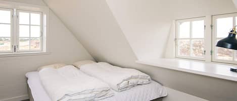 A bedroom with a loft bed, a desk, and a window with a view of buildings.