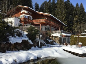 Un edificio de estilo chalé con balcón de madera, rodeado de árboles nevados y un paisaje rocoso.