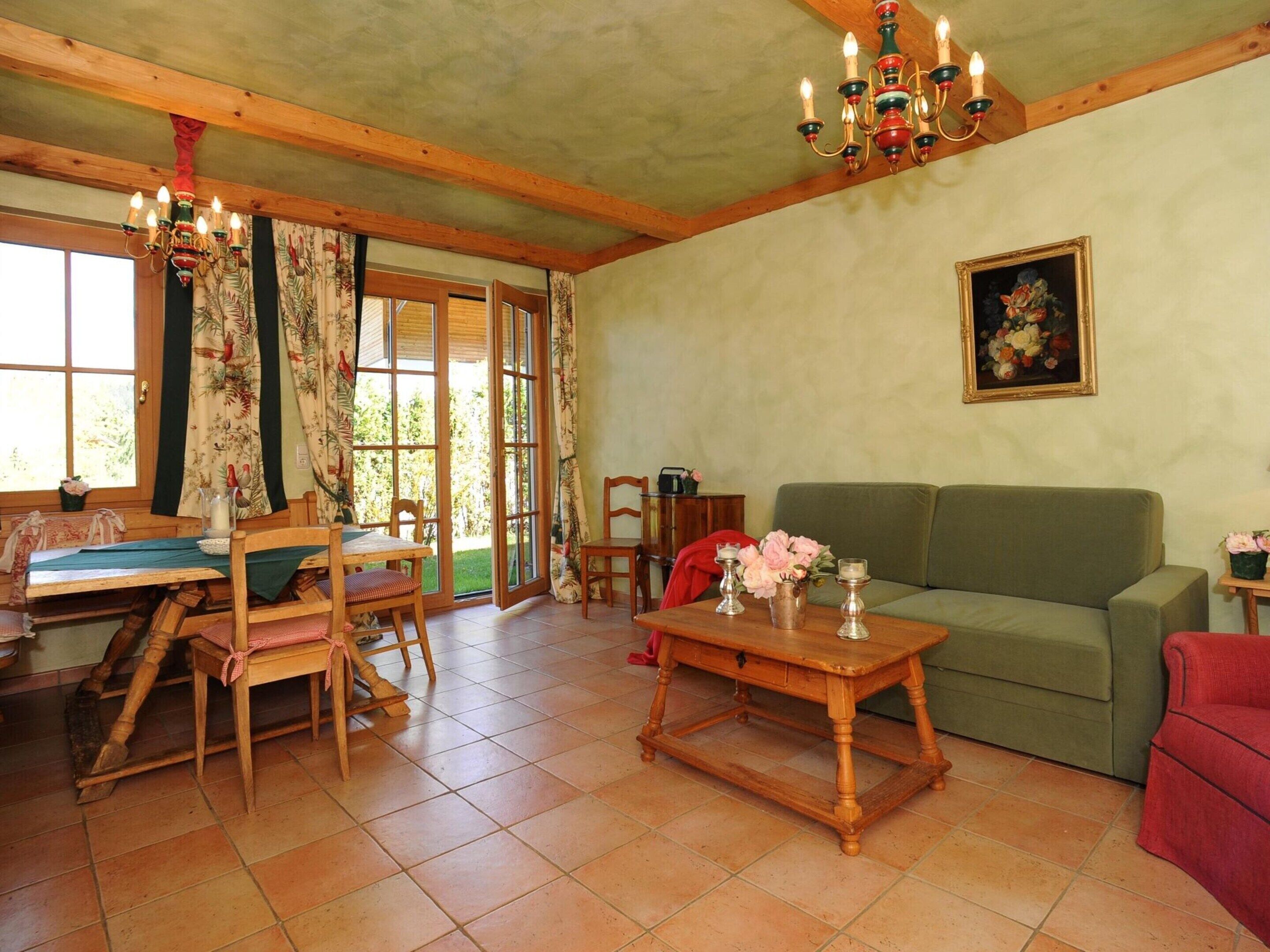 A cozy living room with a wooden table, chairs, a green sofa, and a painting on the wall.