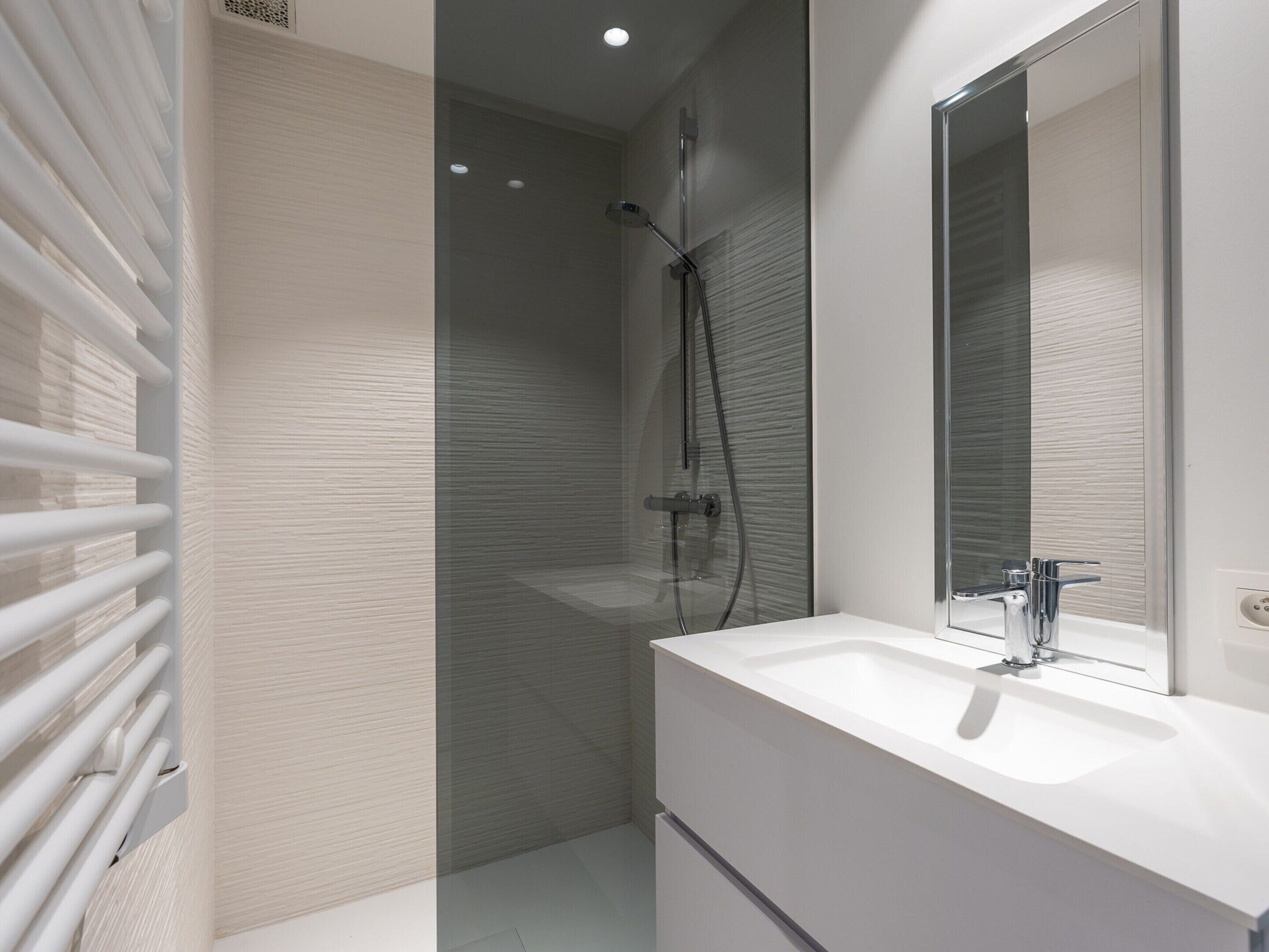 Une salle de bain moderne avec une douche à parois de verre, un meuble-lavabo blanc avec un miroir et un porte-serviettes.
