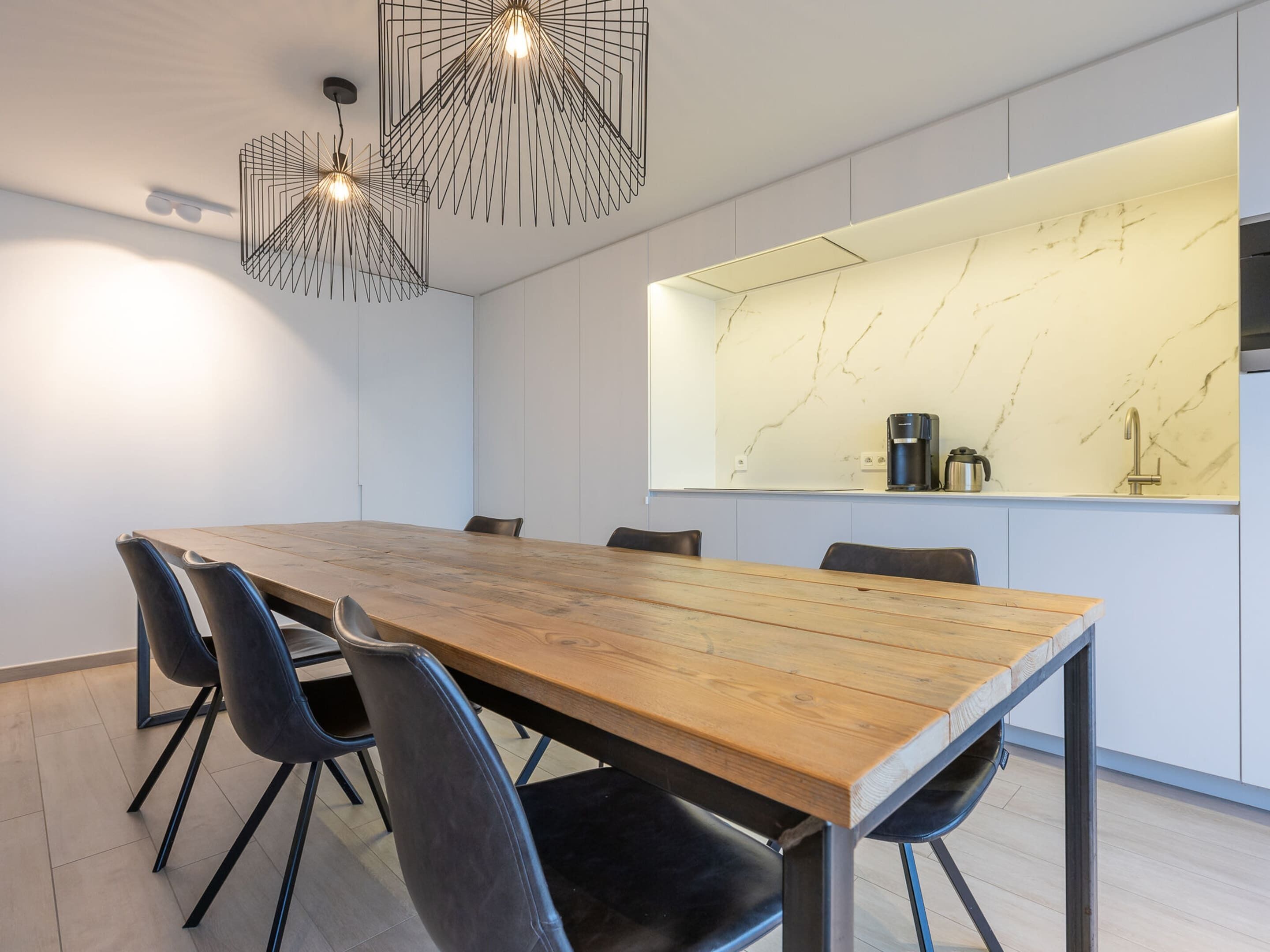 Uma sala de jantar moderna com uma mesa de madeira, cadeiras pretas e um lustre geométrico singular.