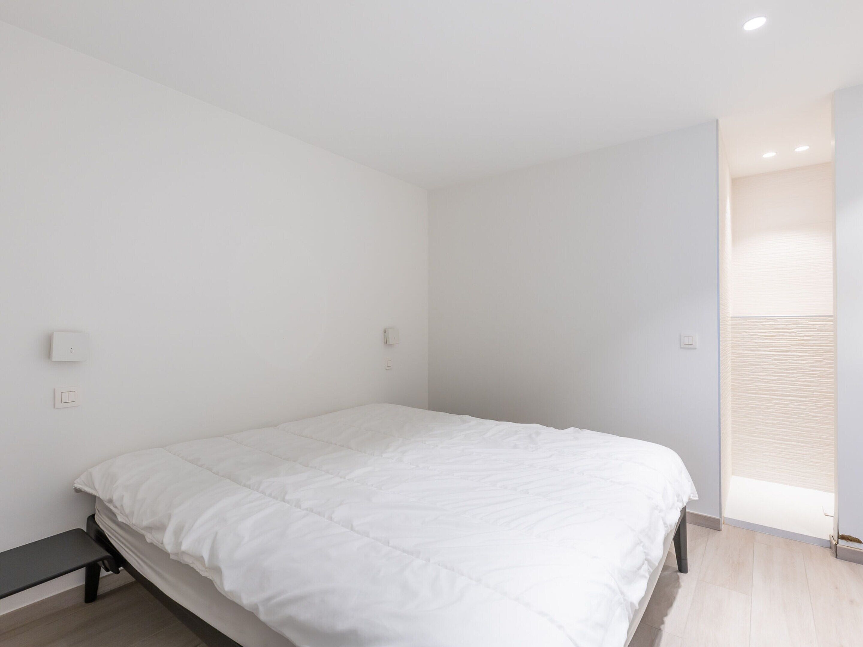 A minimalist bedroom with a single bed, a bench, and a small window.