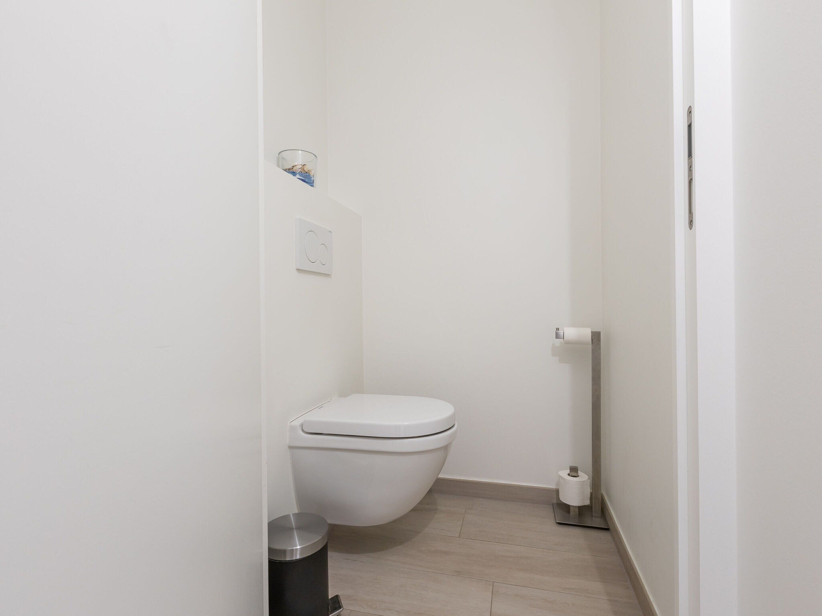 Un baño pequeño y blanco con un inodoro, un bote de basura y un dispensador de papel higiénico.