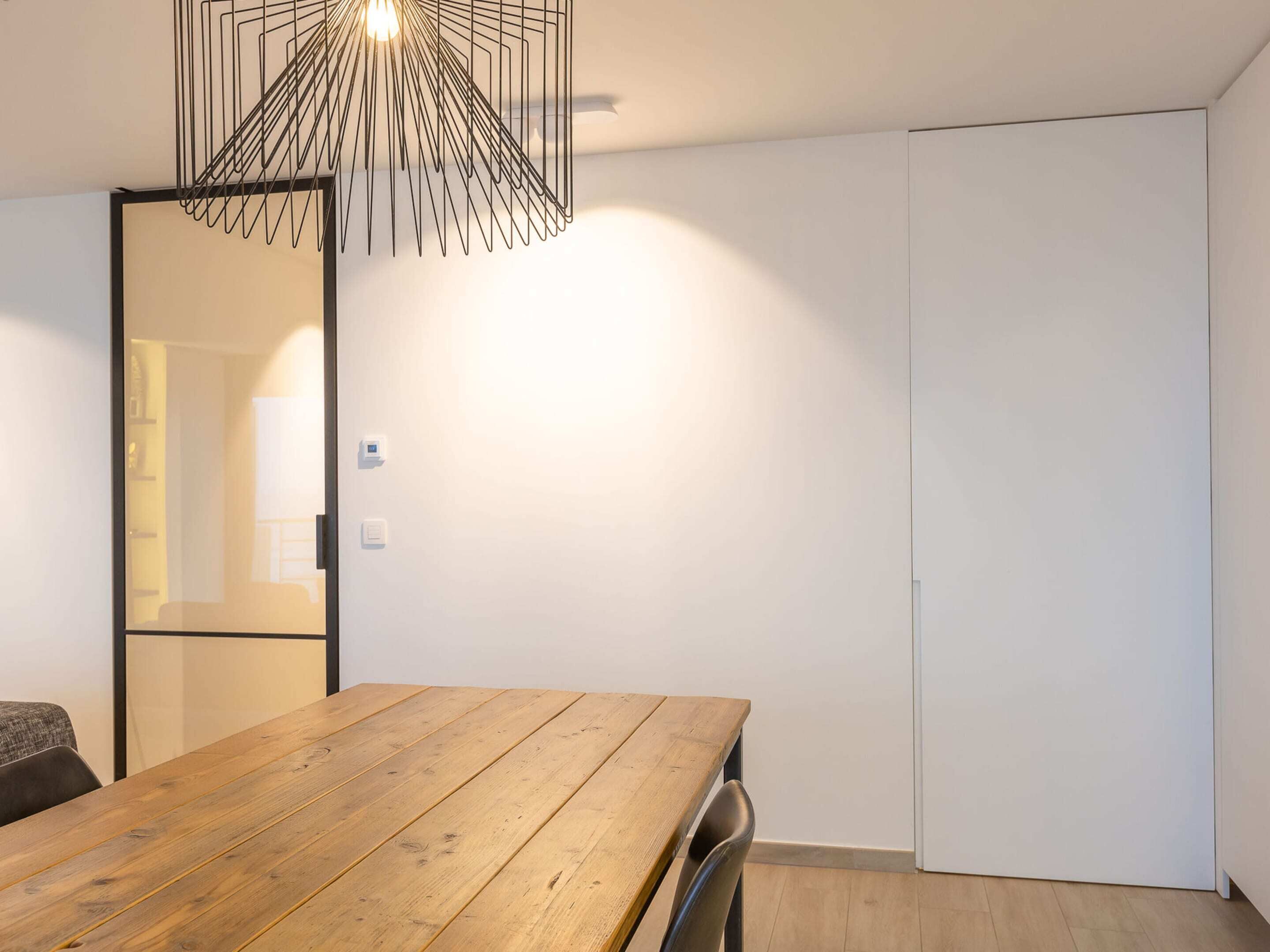 A modern room with a wooden dining table, a mirror, and a white wardrobe.