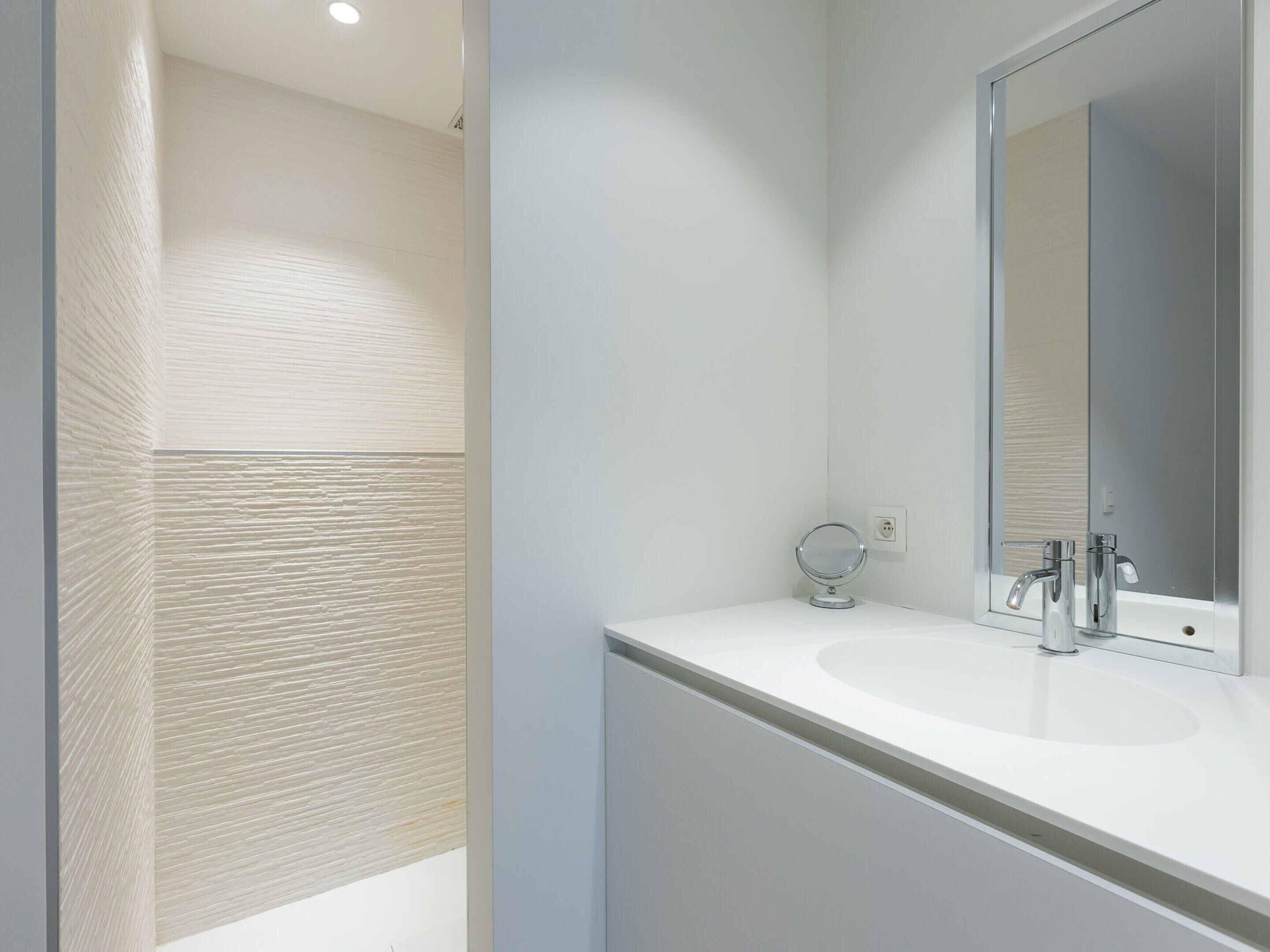 A modern bathroom with a white vanity, a round mirror, and a chrome faucet.