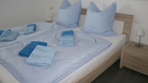 A neatly made bed with blue bedding and pillows, a wooden headboard, and a bedside table with a lamp. - Ostseebrandung - Haus Seestern (Dranske)