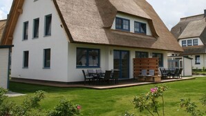 A two-story house with a thatched roof, white exterior walls, and a small front porch with outdoor seating. - Ostseebrandung - Haus Seestern (Dranske)