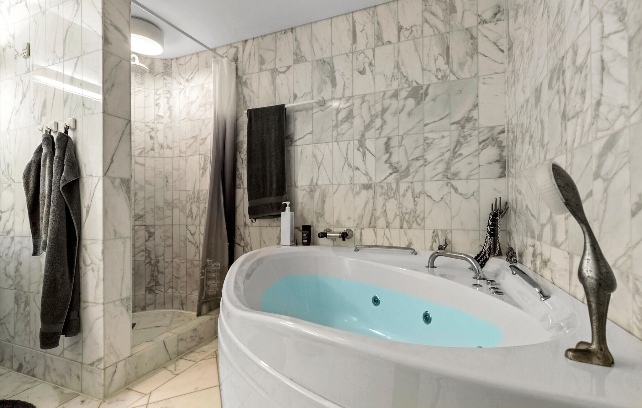 Une salle de bain avec un mur en marbre, une baignoire et un espace douche.