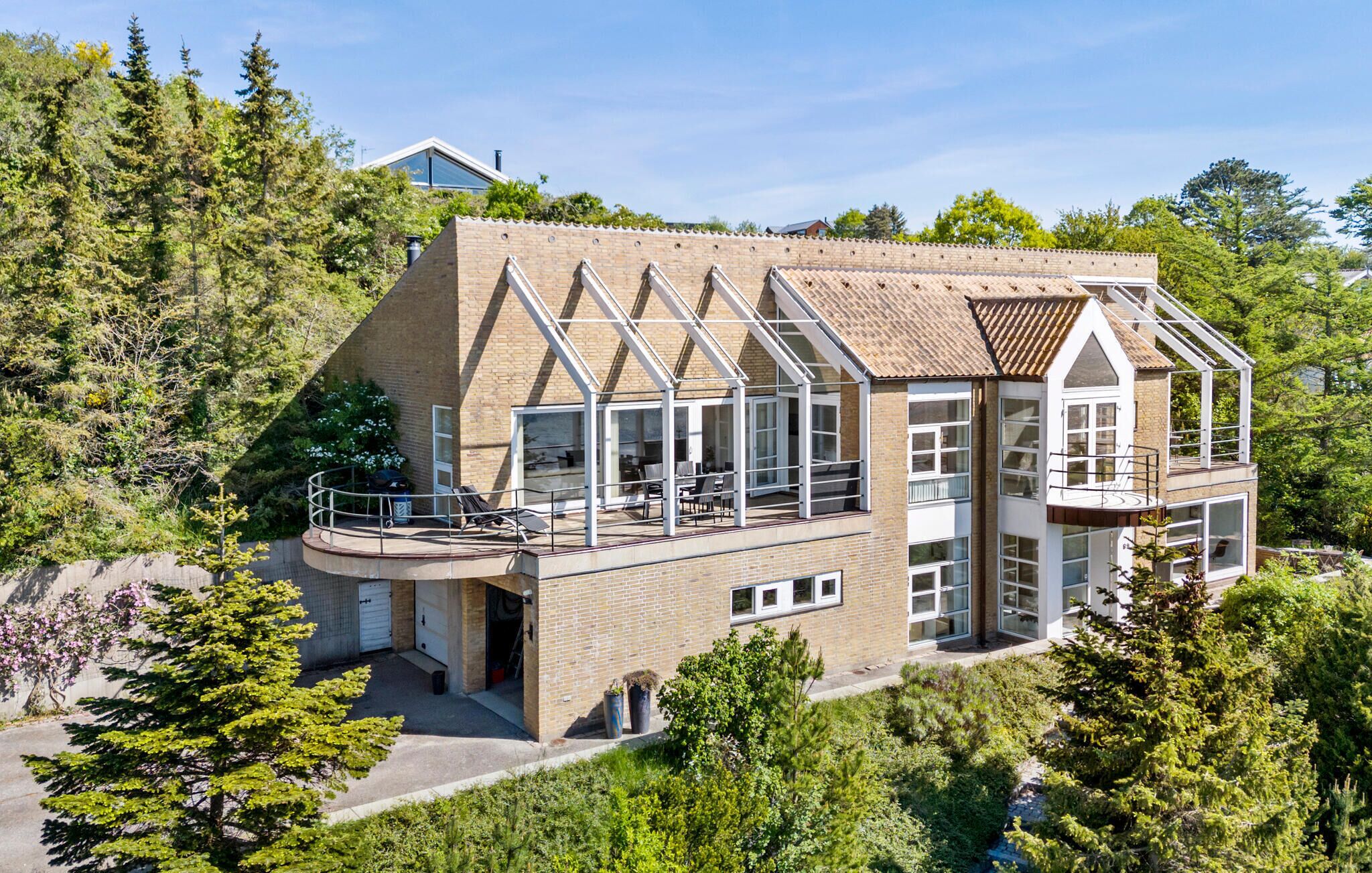 Une maison moderne dotée d’un grand balcon, d’un garage et offrant une vue sur les arbres environnants.