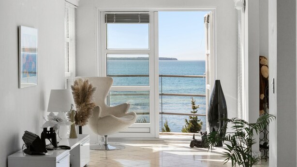 Een moderne kamer met een groot raam met uitzicht op de zee, een comfortabele fauteuil, een bureau met een lamp en een kleine hondenbeeld.