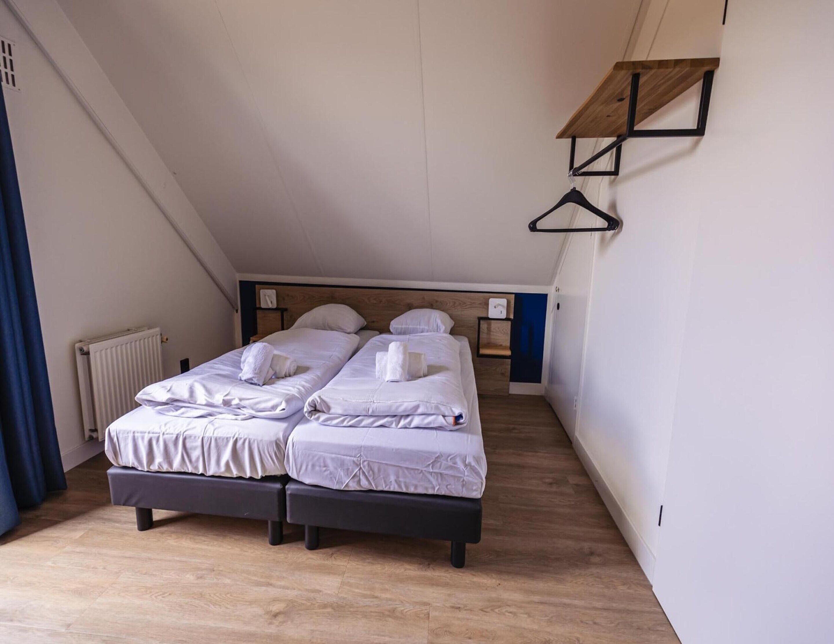 Una camera da letto moderna e accogliente con due letti, pavimento in legno, termosifone e una mensola a parete essenziale.