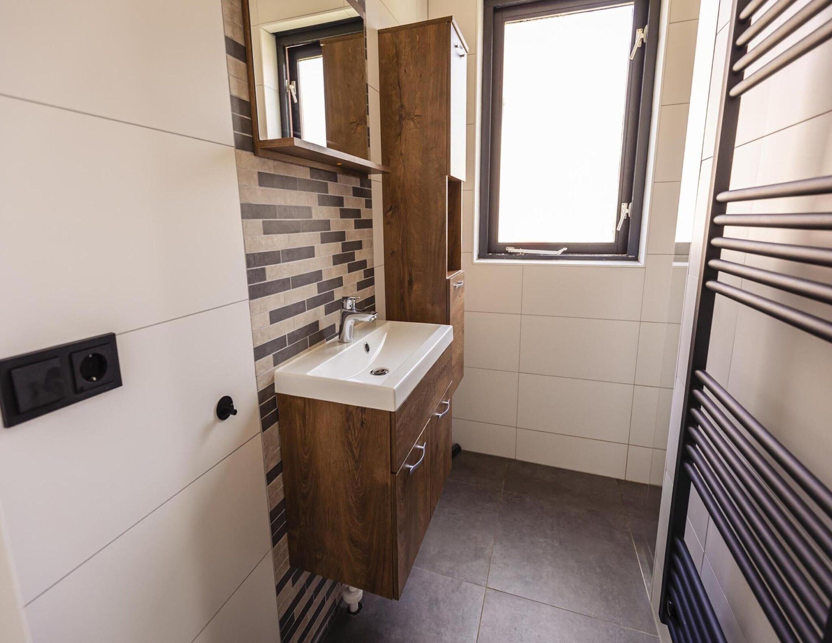 A compact bathroom with a modern sink, wooden vanity, and a window providing natural light.