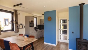 A modern kitchen with a built-in oven and microwave, a dining area with a wooden table and chairs, and a blue accent wall. - Detached Home Nijmegen Lake View Sauna (Ewijk)
