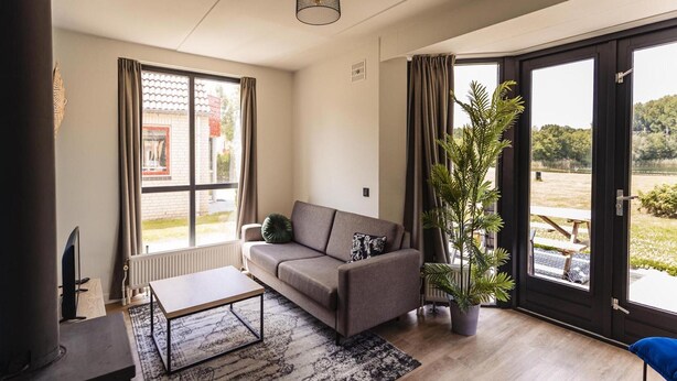 A modern living room with a sofa, coffee table, and a potted plant. - Detached Home Nijmegen Lake View Sauna (Ewijk)