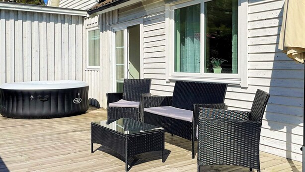 A deck with outdoor furniture, a hot tub, and a house with white siding and a window. - 4 Star Holiday Home in Uddevalla (Uddevalla)