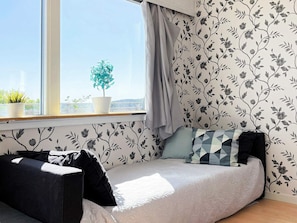 Une pièce avec un lit, une fenêtre avec des rideaux, une plante en pot et un papier peint à motifs floraux.