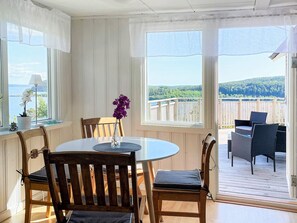 A room with a round table, chairs, a vase with flowers, and a view of a deck and landscape.