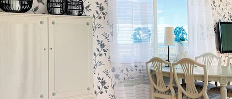 A dining area with a white cabinet, a table with chairs, and a window with sheer curtains.
